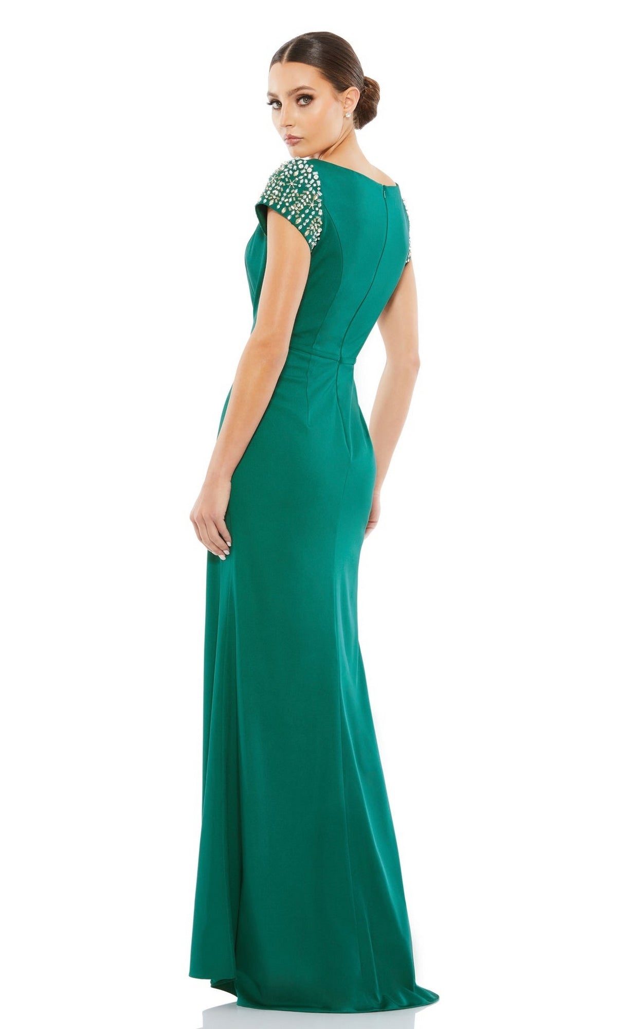 A woman in the Long Formal Dress 55718 by Mac Duggal, an emerald green fitted gown with embellished cap sleeves, stands and looks over her shoulder.